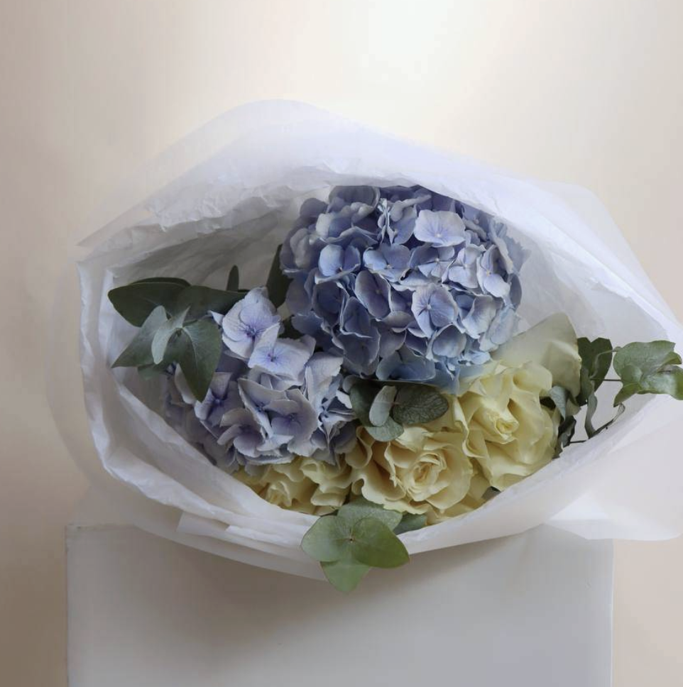 Soft blue hydrangeas and cream roses with eucalyptus in white wrap — Floritta