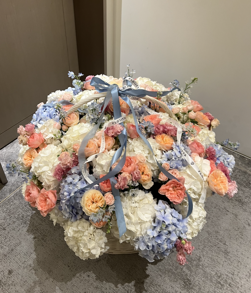 Blush, coral and blue floral arrangement in woven basket with silk ribbon — Floritta
